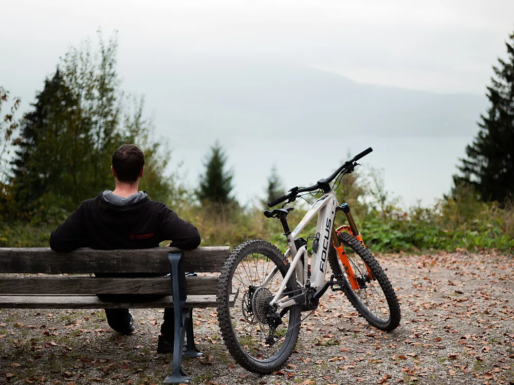 Radfahrer mit E-Bike auf einer Bank mit Blick auf den Tegernsee